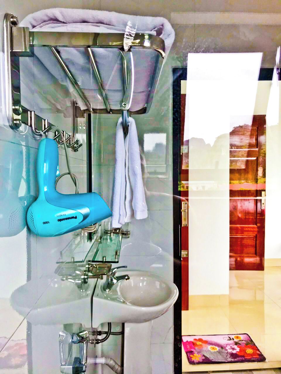 A bathroom with a glass sink, a blue handheld showerhead, and a towel rack.