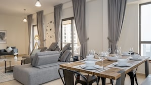 A modern living room with a grey sofa, a wooden dining table set for six, and a large window with curtains. - HiGuests - Sadaf 6 (Dubai)