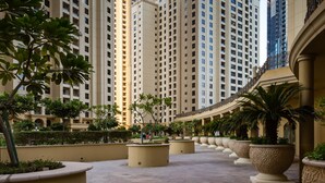 A modern high-rise building with a central courtyard featuring potted plants and a paved walkway. - HiGuests - Sadaf 6 (Dubai)