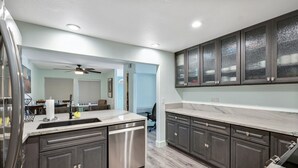A modern kitchen with dark cabinetry, a stainless steel dishwasher, and a marble countertop. - San Clemente / Dana Point- (San Clemente)