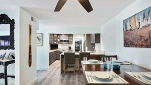 A modern kitchen with dark cabinets, a central island, and a dining area with a wooden table set for four. - San Clemente / Dana Point- (San Clemente)