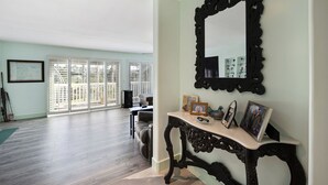 A spacious living area with a large mirror, a console table with framed photos, and a view through a sliding glass door to an outdoor patio. - San Clemente / Dana Point- (San Clemente)