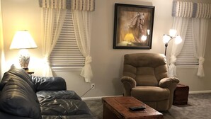 Una sala de estar con un sofá azul, un sillón color beige, una mesa de centro de madera y un cuadro en la pared.