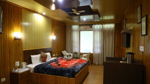Una habitación de hotel con paneles de madera, una cama con colcha estampada y un escritorio con hervidor, además de un ventilador de techo.