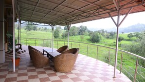Un espacio de estar al aire libre con techo, suelo a cuadros, mobiliario de mimbre y vistas a un paisaje verde.