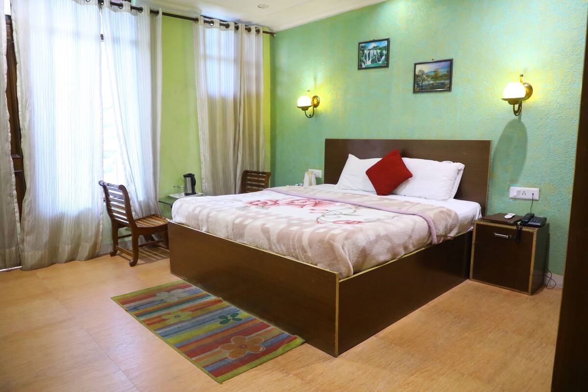 A hotel room with a bed, a chair, a nightstand, a lamp, and a window with curtains.