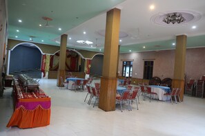 A banquet hall with tables set for events, high ceilings with chandeliers, and a stage area.