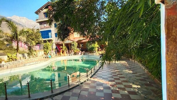 Zona de piscina con un sendero a cuadros, rodeada de edificios y follaje.