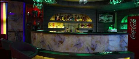 Una zona de bar con mostrador de mármol, estantes llenos de botellas y un cartel de Coca-Cola.