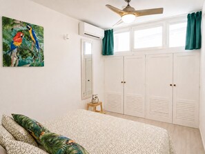 Una camera da letto con un letto, una ventola a soffitto, un condizionatore d'aria, un armadio e un quadro raffigurante pappagalli.