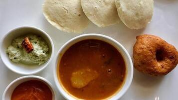 A plate with three idlis, two chutneys, a bowl of sambar, and a fried snack.