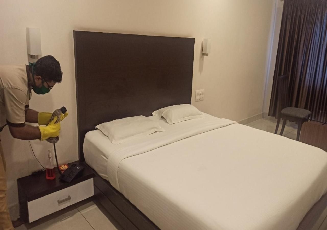 A hotel room with a bed, a nightstand, and a person cleaning the floor.