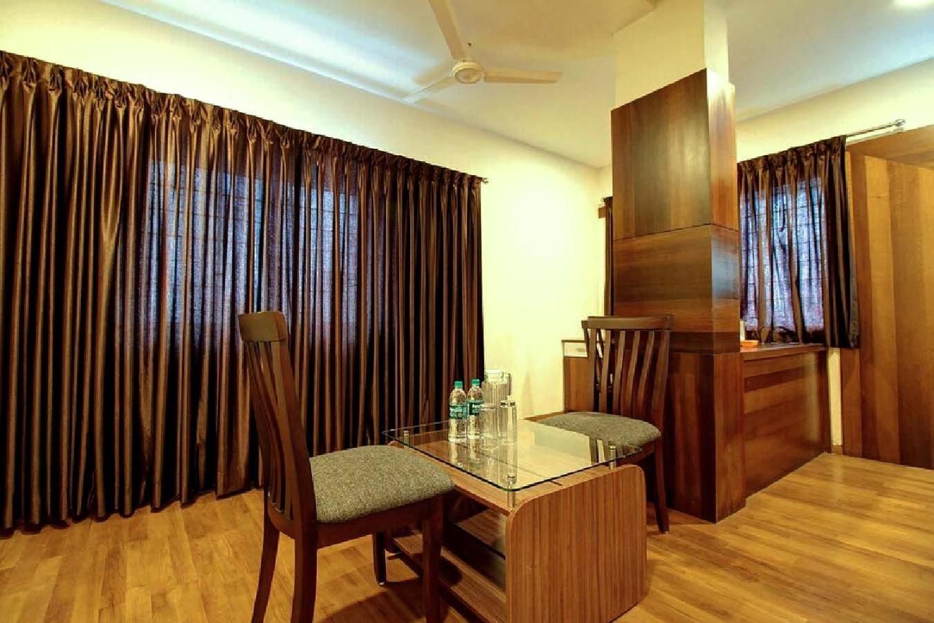 A room with a glass-top table, two chairs, a ceiling fan, and wooden curtains.