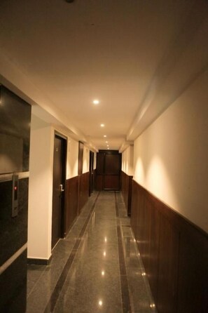 A long, narrow hallway with a polished floor and wooden paneling on the walls. - Traders Hotel (Mangaluru)