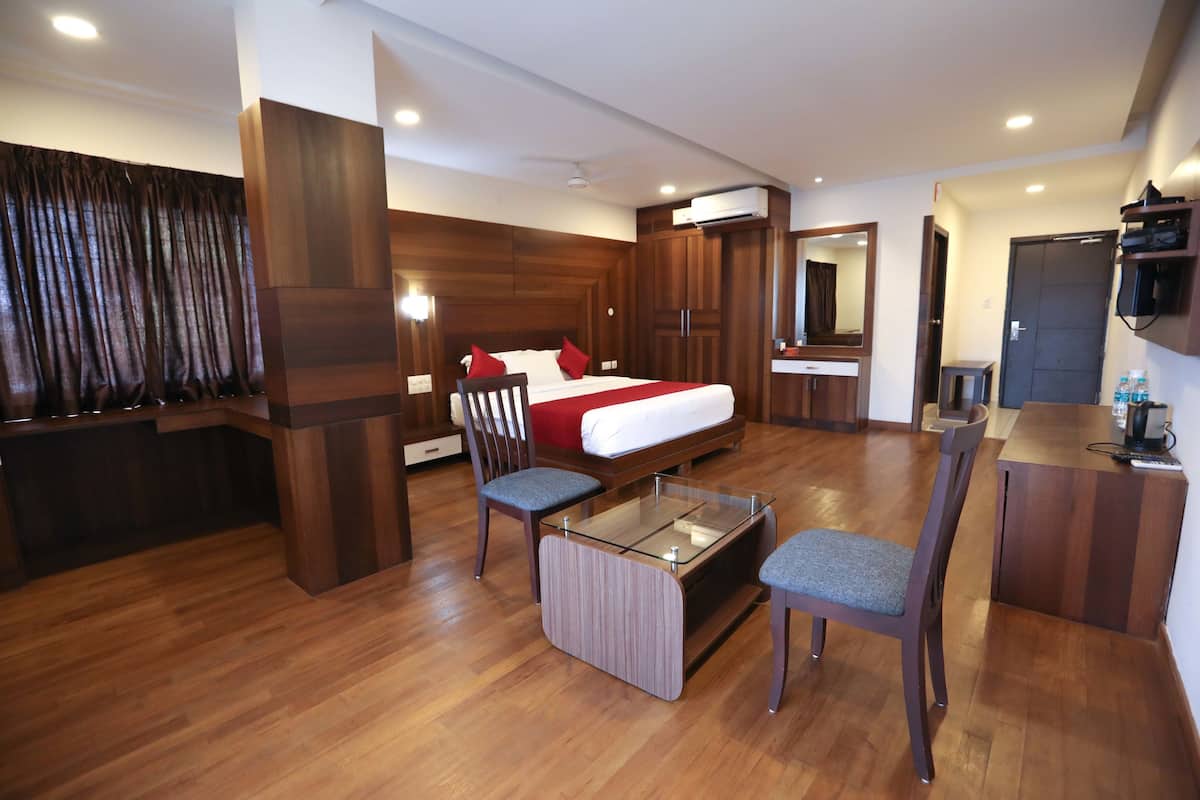 Habitación de hotel con cama, escritorio, dos sillas, una mesa de vidrio, espejo y armario.
