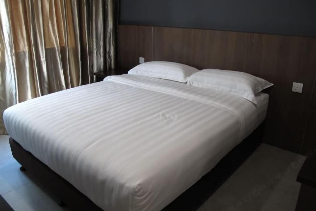 Una cama bien tendida con sábanas blancas en una habitación con paneles de madera y una cortina en la ventana.