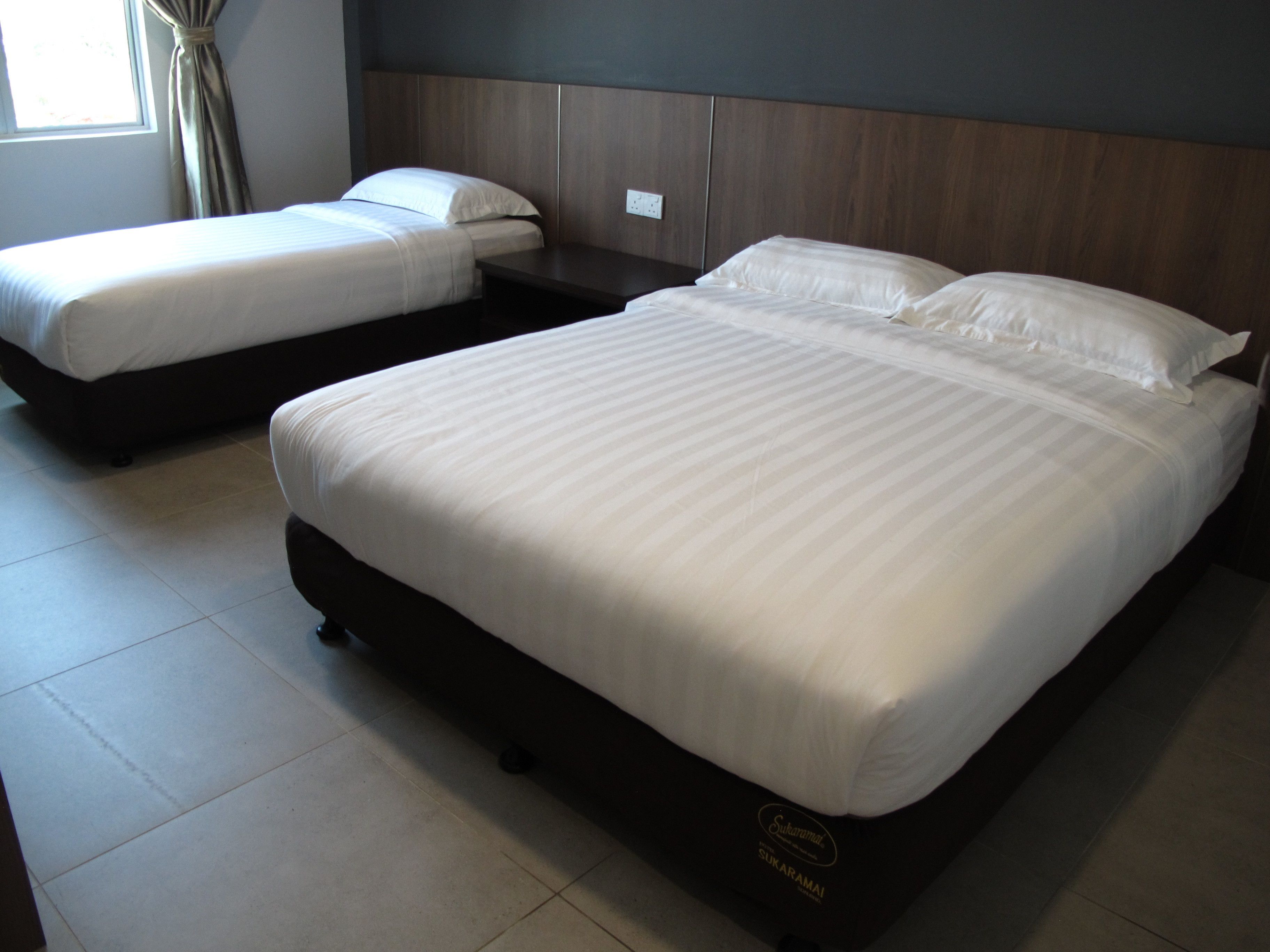 Een hotelkamer met twee bedden, een donker hoofdeinde en een betegelde vloer.