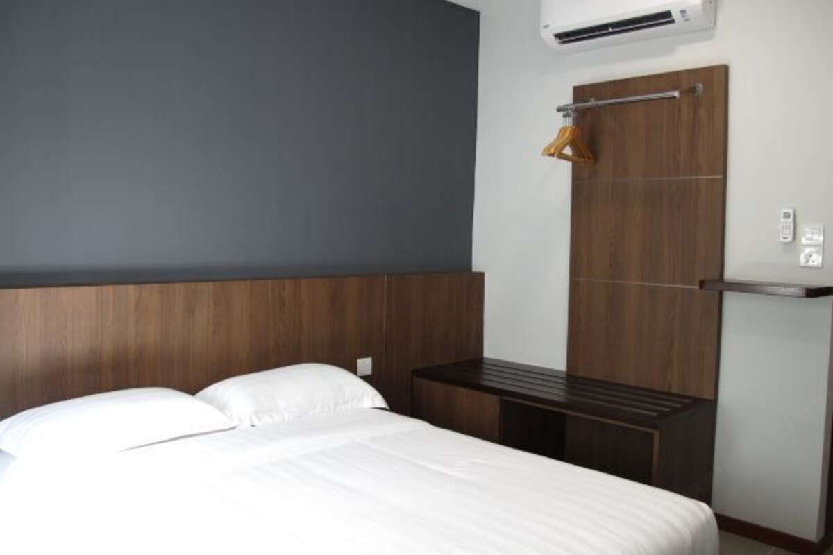 Habitación de hotel con cama, cabecera de madera, escritorio pequeño y aire acondicionado instalado en la pared.