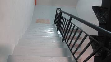 Una escalera con barandilla de metal negro, escalones blancos y una pared roja en la parte superior.