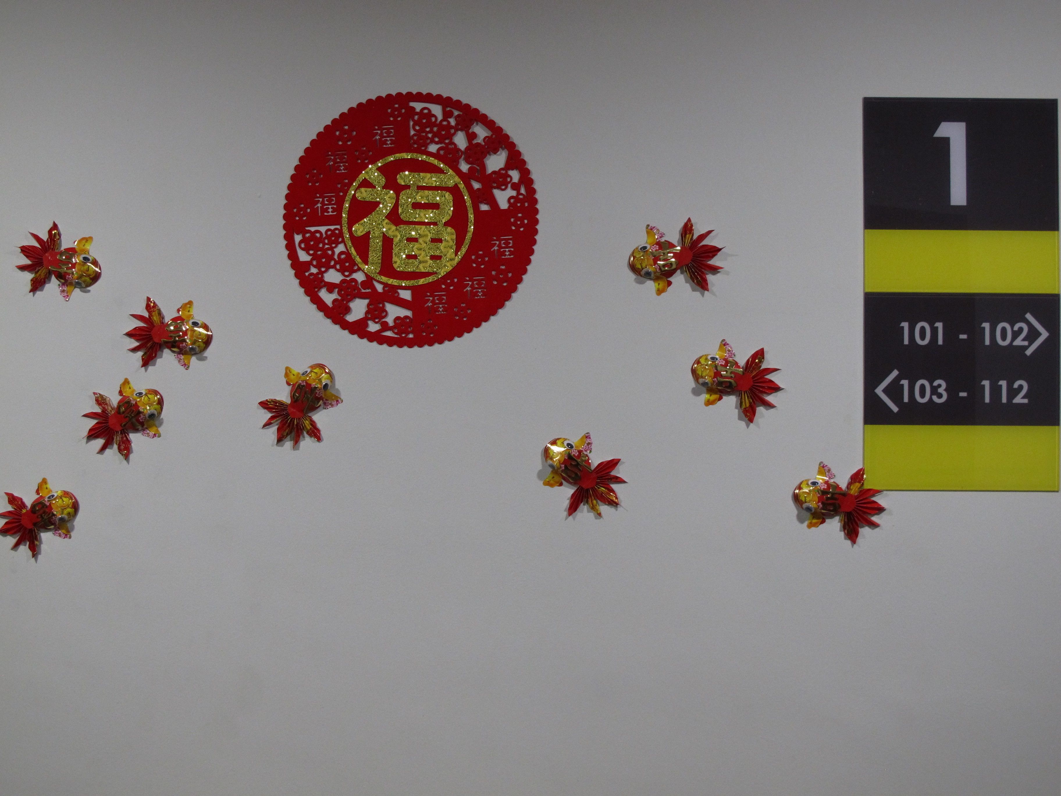 A wall with a red circular decoration featuring Chinese characters, surrounded by small golden fish ornaments. A sign with room numbers is also visible.