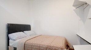 A small, simple room with a bed, a bedside table, and a wall-mounted shelf. - Rumah Kayu Manis Tebet (Jakarta)