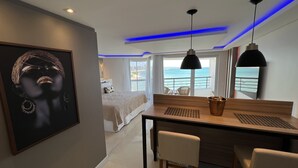 Ein modernes Hotelzimmer mit einem großen Bett, einem Schreibtisch mit zwei Stühlen, Meerblick und einem gerahmten Kunstwerk an der Wand.