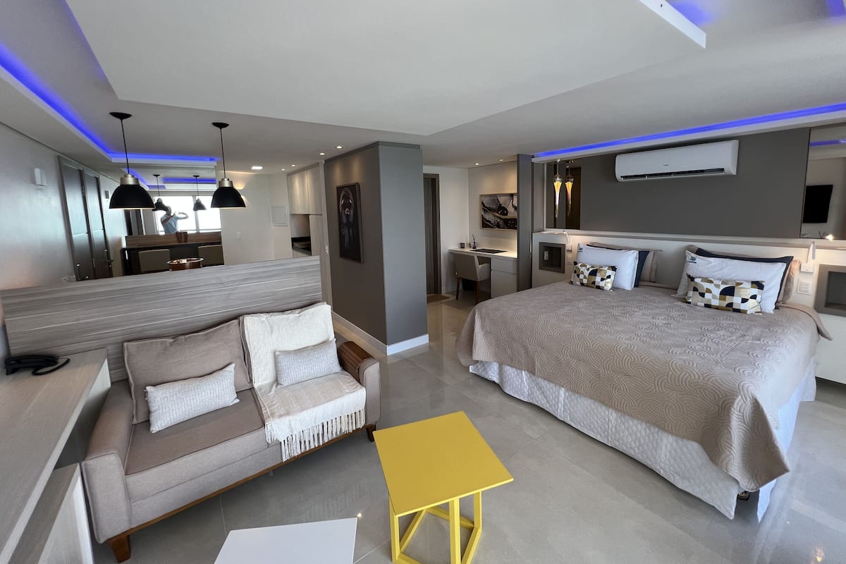 Una habitación de hotel moderna con sofá, cama, mesita de noche y escritorio con silla.