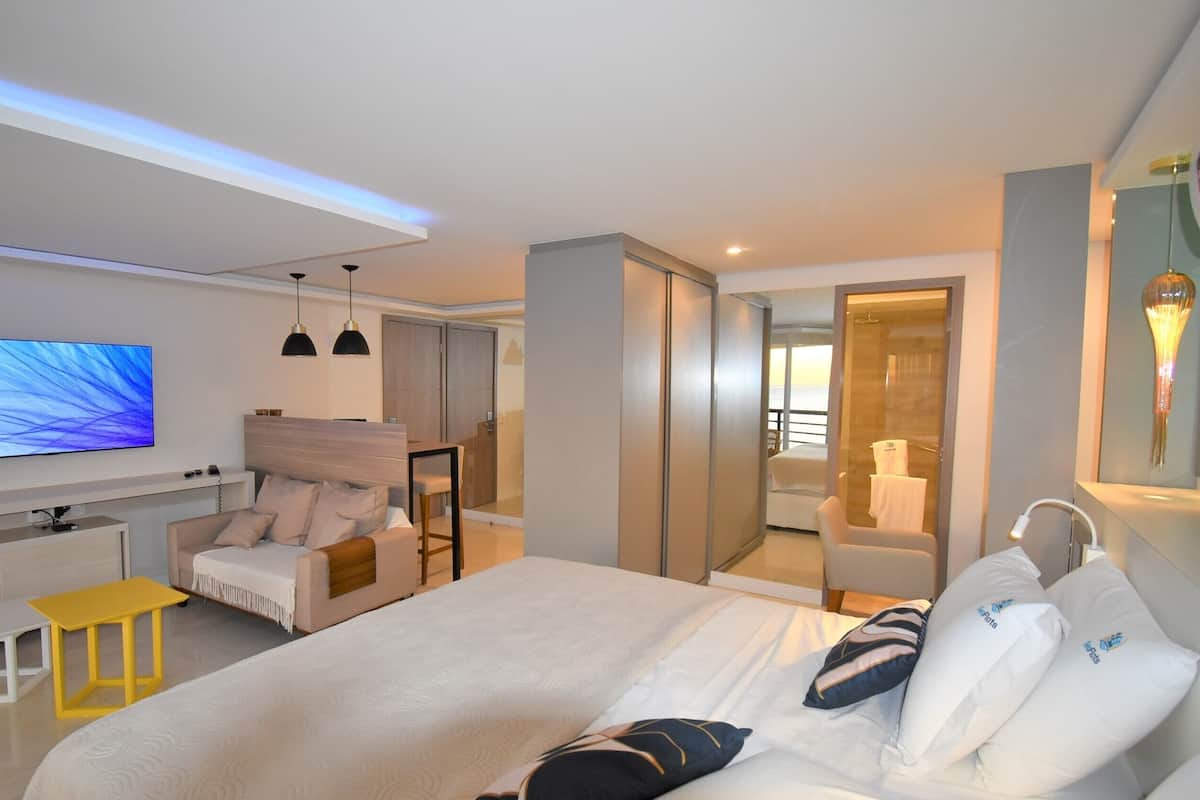 Una habitación de hotel moderna con una cama grande, televisión, escritorio y baño con ducha y espejo.
