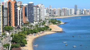 A coastal cityscape with high-rise buildings, a sandy beach, and numerous boats in the water.