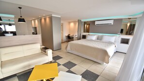 A modern hotel room with a large bed, a sofa, a small table, a desk, and a bathroom.