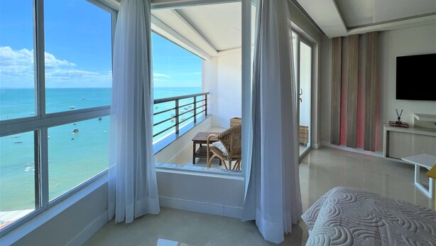 Ein modernes Hotelzimmer mit Balkon und Meerblick, inklusive Bett, Fernseher und einem kleinen Tisch mit Stühlen.