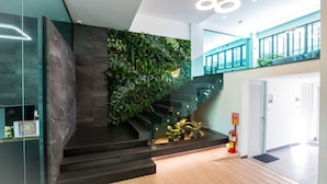 Un escalier moderne avec une rampe en verre, un mur végétal et un extincteur sur la plateforme.