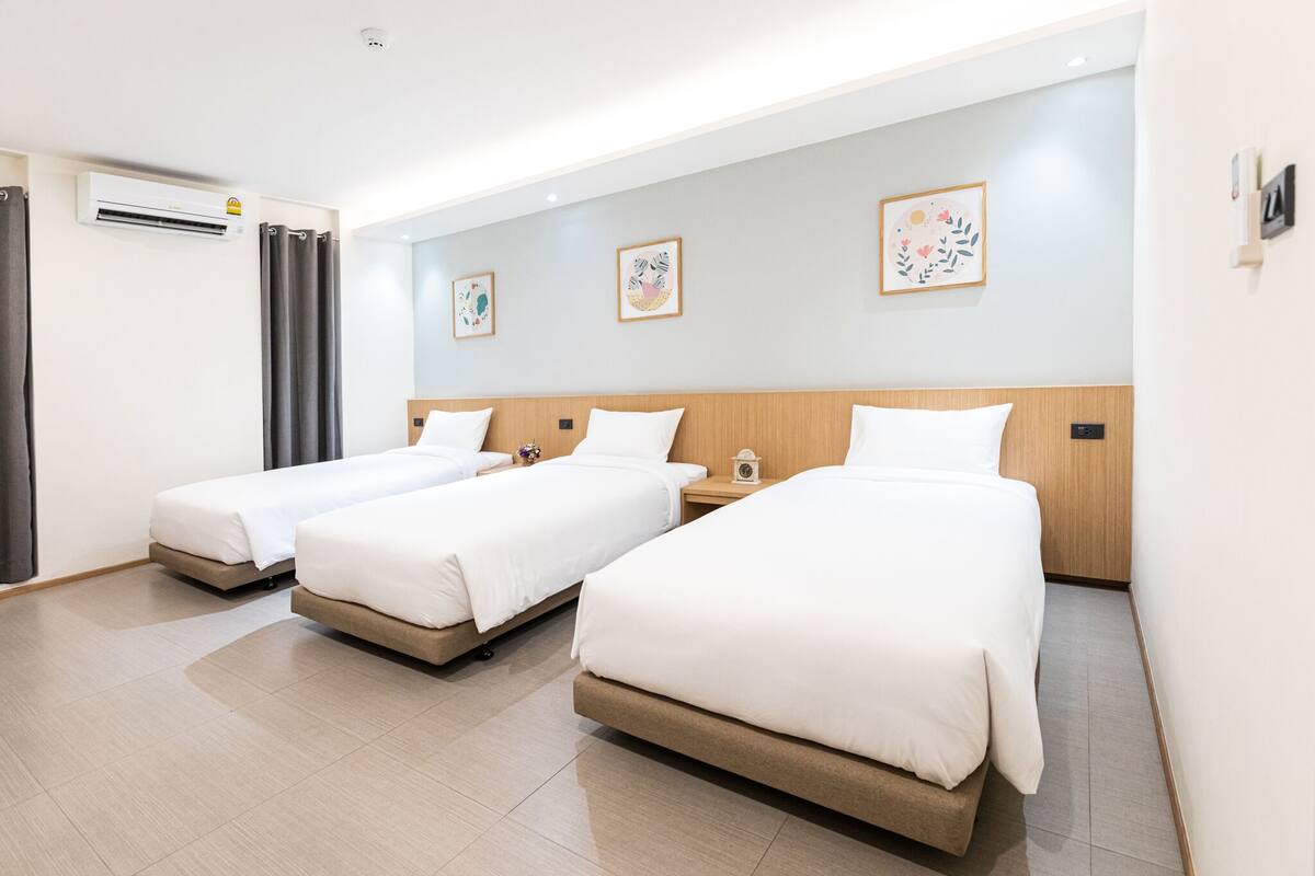A hotel room with three beds, an air conditioning unit, and artwork on the walls.