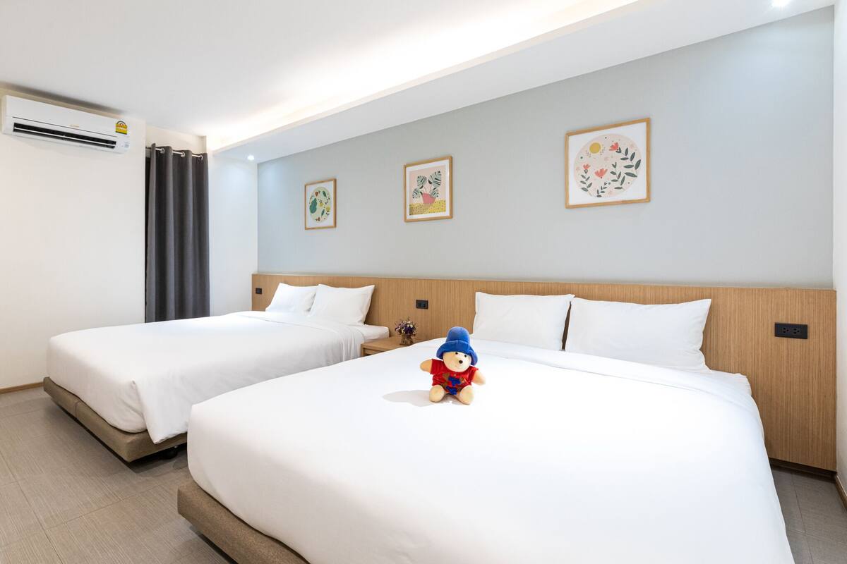 A hotel room with two beds, a wooden headboard, a small table, and a wall-mounted air conditioner.