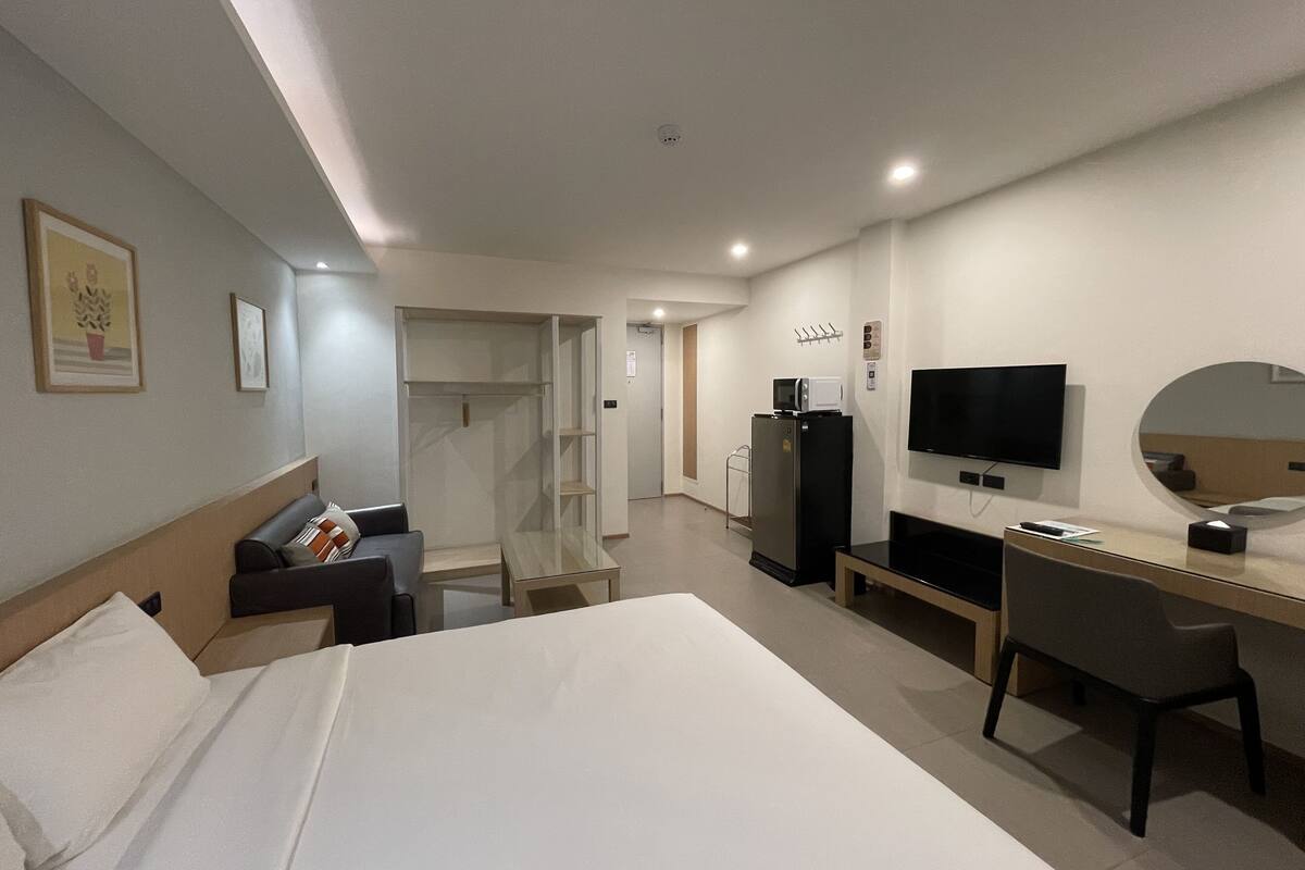 A hotel room with a bed, a desk, a chair, a TV, a mirror, and a wardrobe.