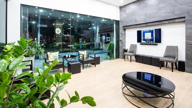 Un espace de bureau moderne avec des murs en verre, un coin salon avec des canapés et des fauteuils, et un écran de télévision fixé au mur.