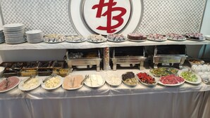 Una mesa de buffet con diversos alimentos y utensilios, incluyendo platos, fuentes y recipientes.