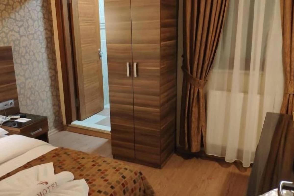 A hotel room with a bed, a wardrobe, a bedside table with a phone, and a shower area.