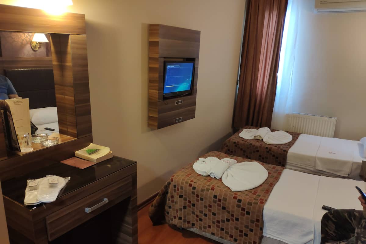 A hotel room with a wooden dresser, a flat-screen TV mounted on the wall, two beds with towels, and a mirror.