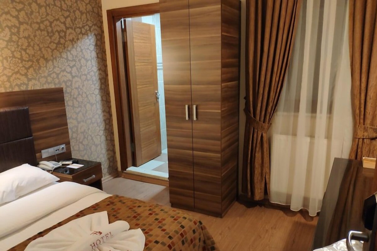 Una habitación de hotel con una cama, un armario, una mesita de noche y la puerta del baño.