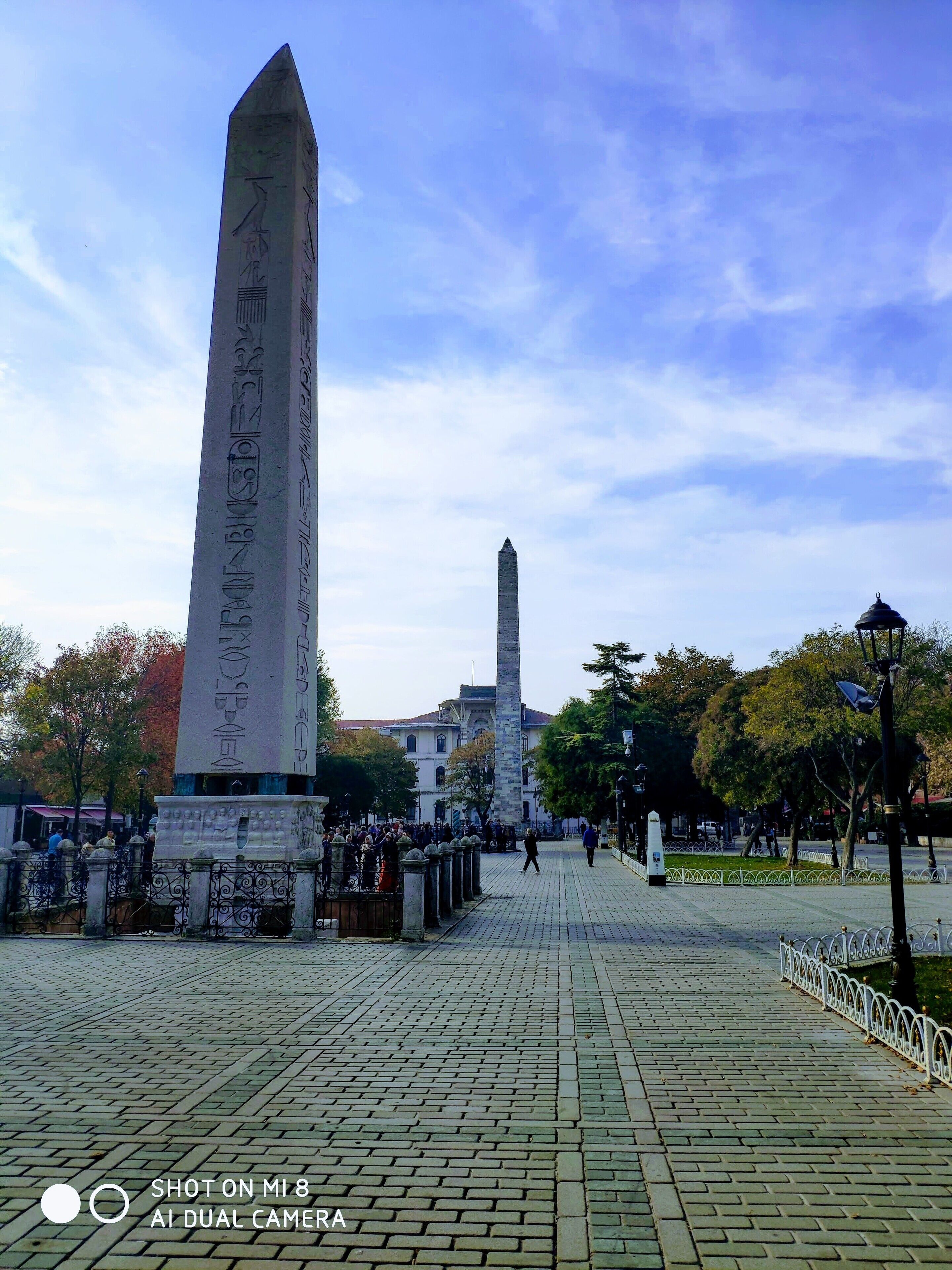 A monument with inscriptions, a paved walkway, and a distant building.