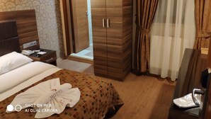 Habitación de hotel con cama, armario de madera, mesita de noche con teléfono y baño visible a través de una puerta abierta.