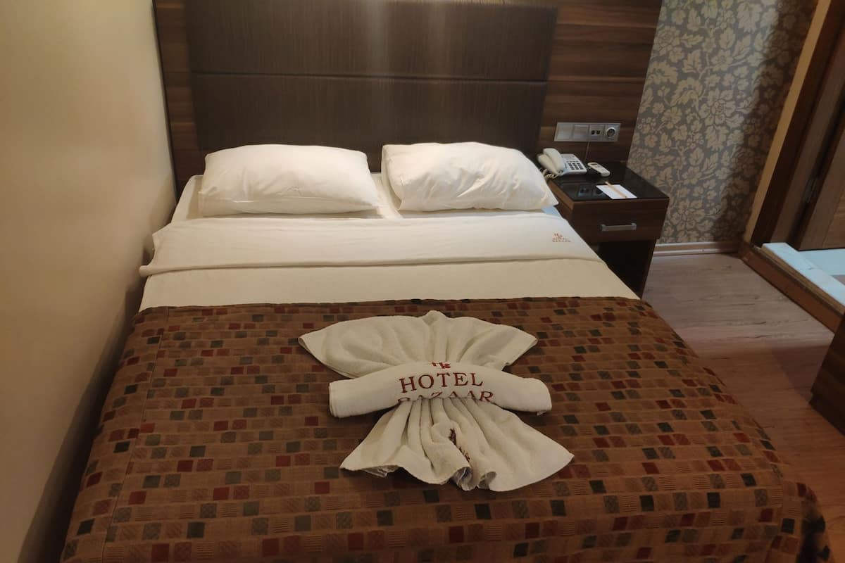 A hotel room with a bed, pillows, a telephone, and a folded towel with 'HOTEL ZAAAR' on it.