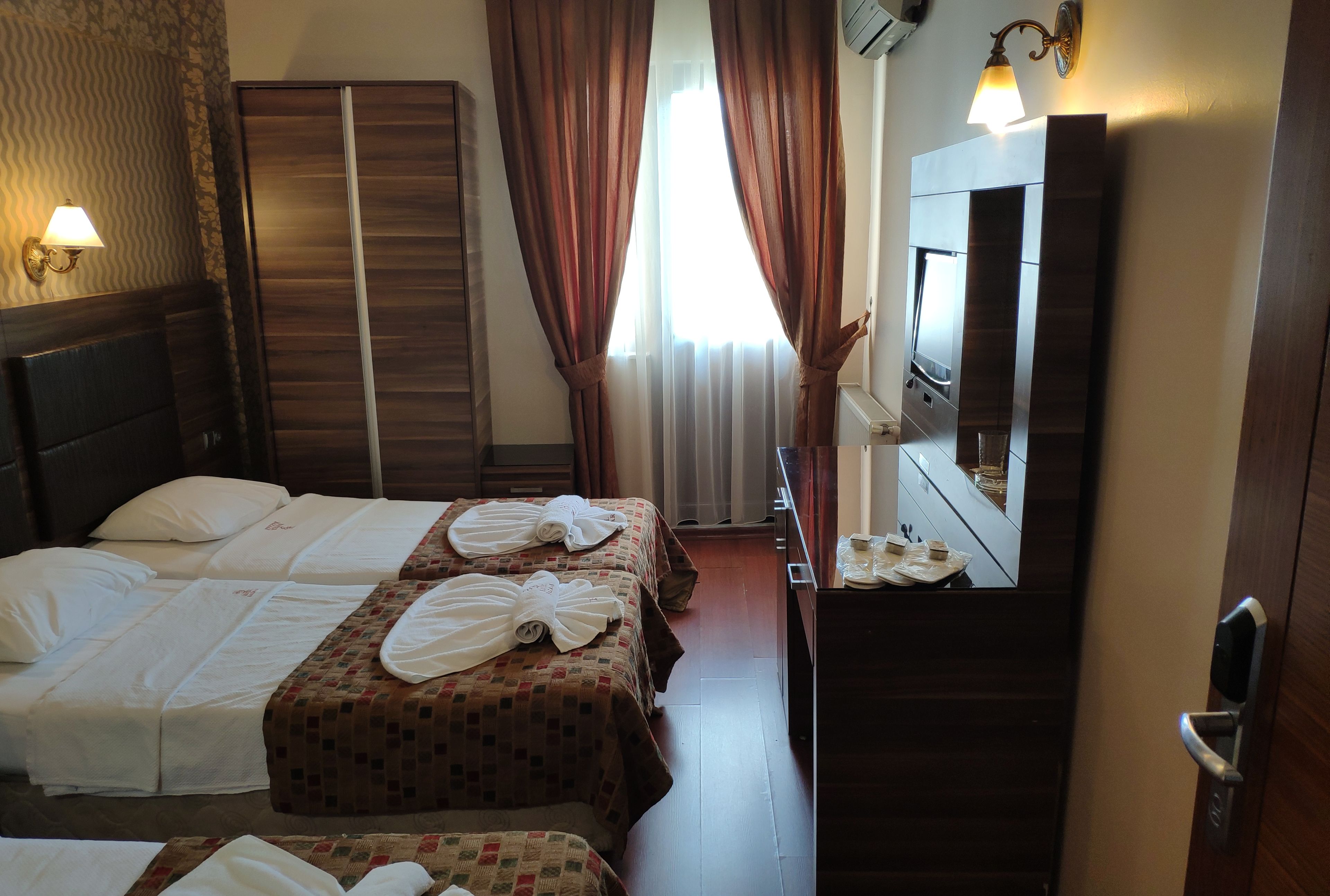 A hotel room with two beds, a large mirror, a dresser, and a window with curtains.