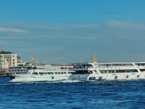 A ferry with multiple decks and passengers, docked at a port with industrial buildings and cranes in the background. - Hotel Bazaar (Istanbul)