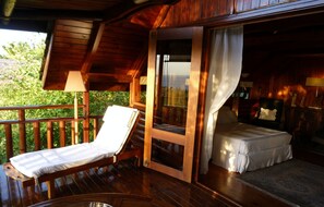 A wooden deck with a lounge chair, a bed with a white bedspread, and a glass door leading to a bedroom. - Senteur Vanille (Saint-Paul)