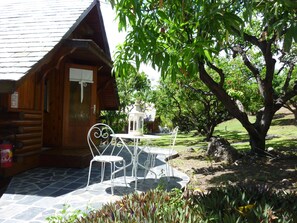 A wooden cabin with a stone patio, white metal chairs, and a lantern. - Senteur Vanille (Saint-Paul)