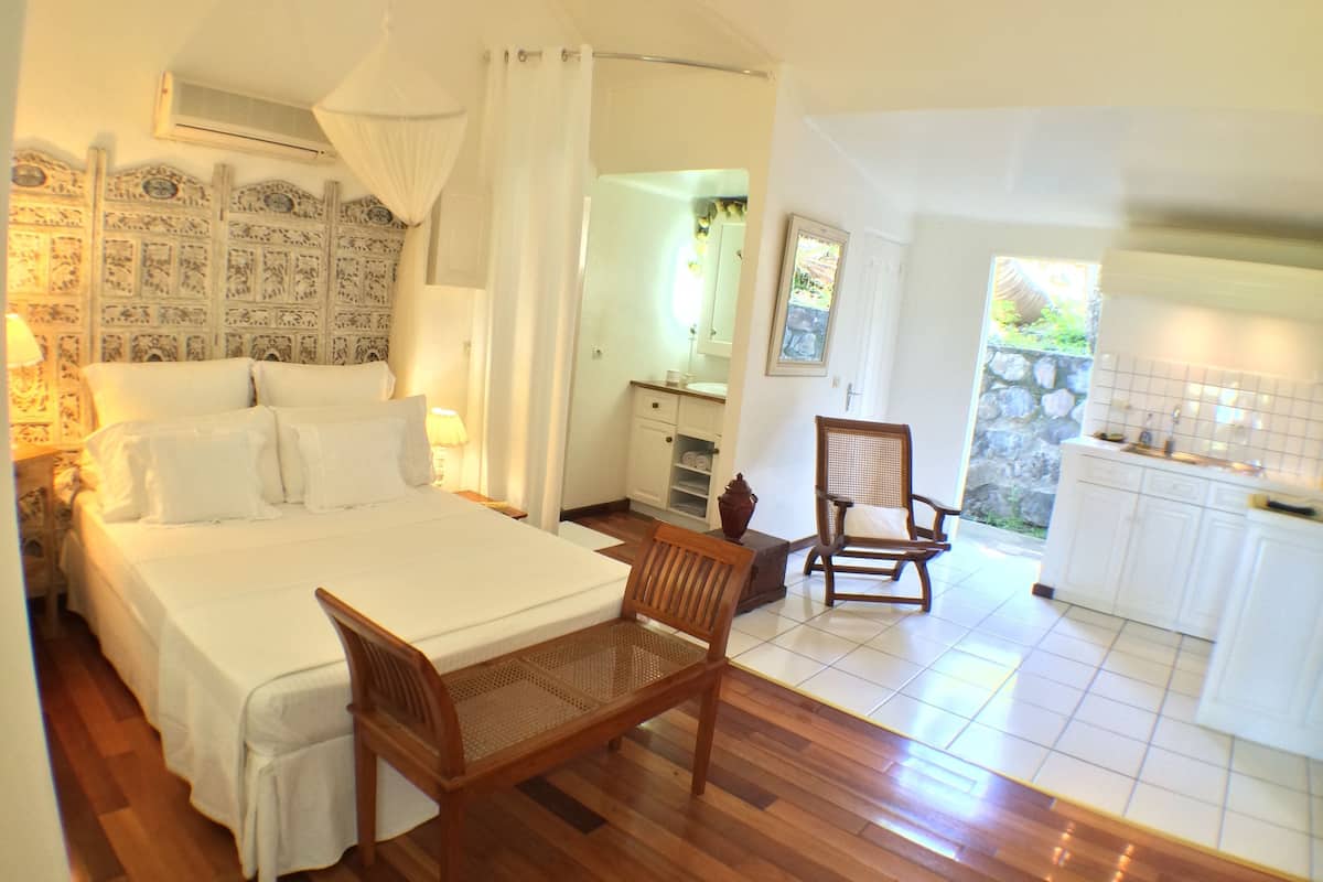 A bedroom with a bed, a wooden chair, a small table, and a bathroom visible through an open door.