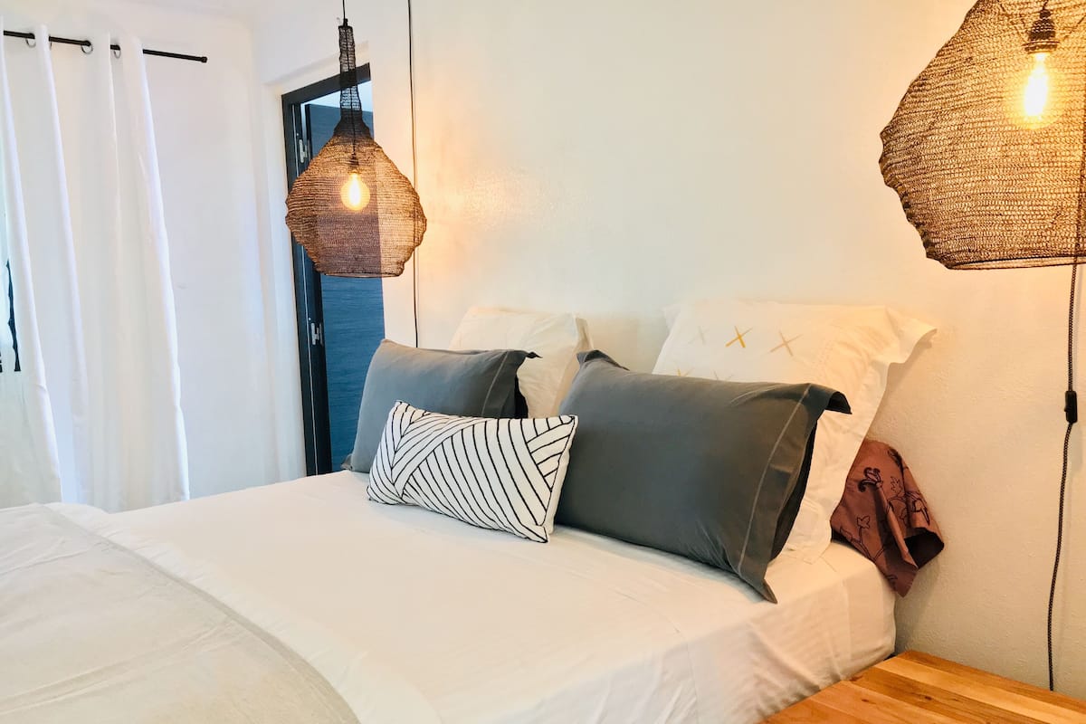 A bed with white bedding, multiple pillows, and two hanging light fixtures.