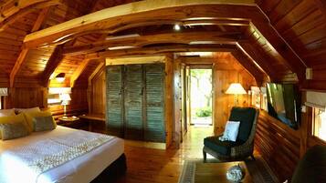 A cozy log cabin bedroom with a large bed, a chair, and a TV.